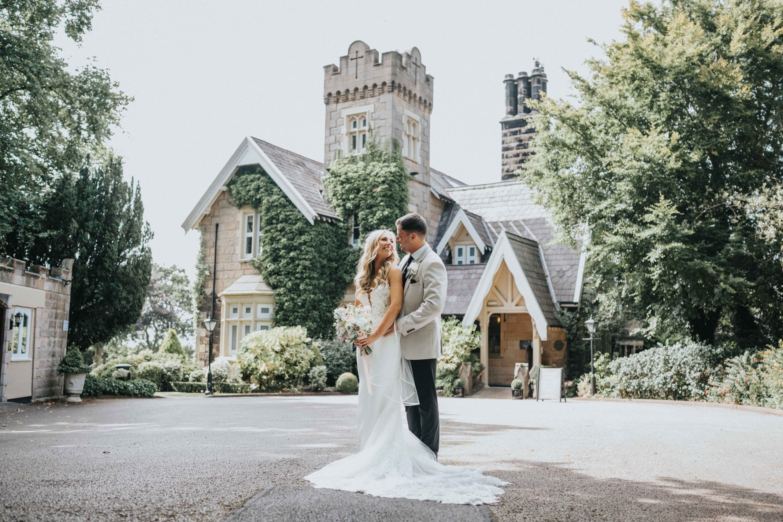 A bride and groom standing in front of the west tower main house, embracing each other on a sunny day