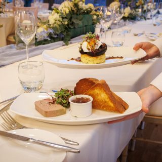 Waiting staff serving plated starters and desserts along a dressed wedding breakfast table in the Ballroom at West Tower.