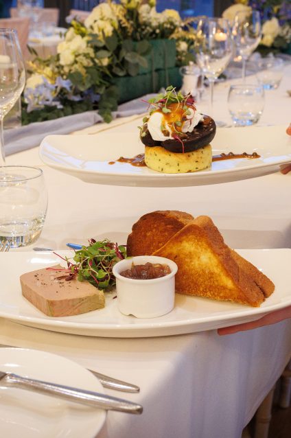 Waiting staff serving plated starters and desserts along a dressed wedding breakfast table in the Ballroom at West Tower.