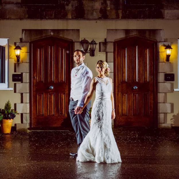 Bride and groom standing hand in hand outside the front doors of the West Tower cottages at night.