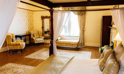 Spacious Bridal Suite at West Tower with a four poster bed, chaise longue, armchairs and patterned rugs on a wooden floor.