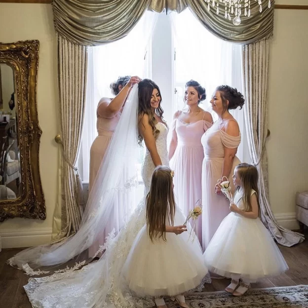 Bride in the Bridal Suite at West Tower surrounded by bridesmaids and two flower girls as they adjust her veil by the window.