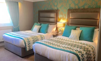 Coach House bedroom at West Tower with two double beds, teal cushions and patterned throws against a feature wall.