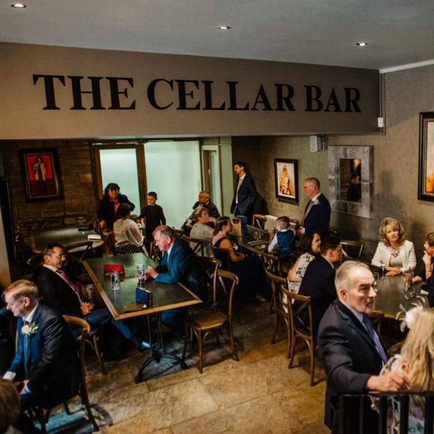 Wedding guests gathered in the Cellar Bar at West Tower, chatting around tables beneath “The Cellar Bar” sign.