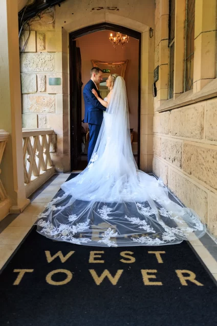 Bride and groom standing on the West Tower entrance mat beneath the stone archway, her long veil flowing behind them.
