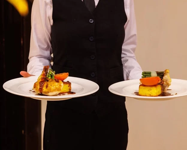 Member of the West Tower team serving plated wedding breakfast main courses on two white plates.