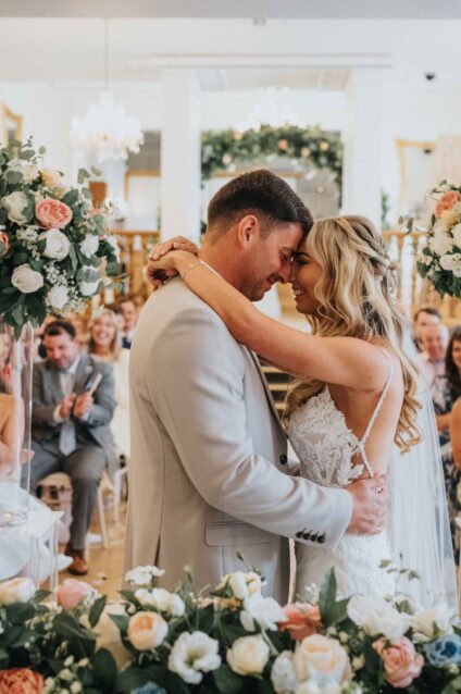 Bride and Groom embracing eachother as they've just tied the know at West Tower in teh ballroom surrounded by family and friends sitting behind them